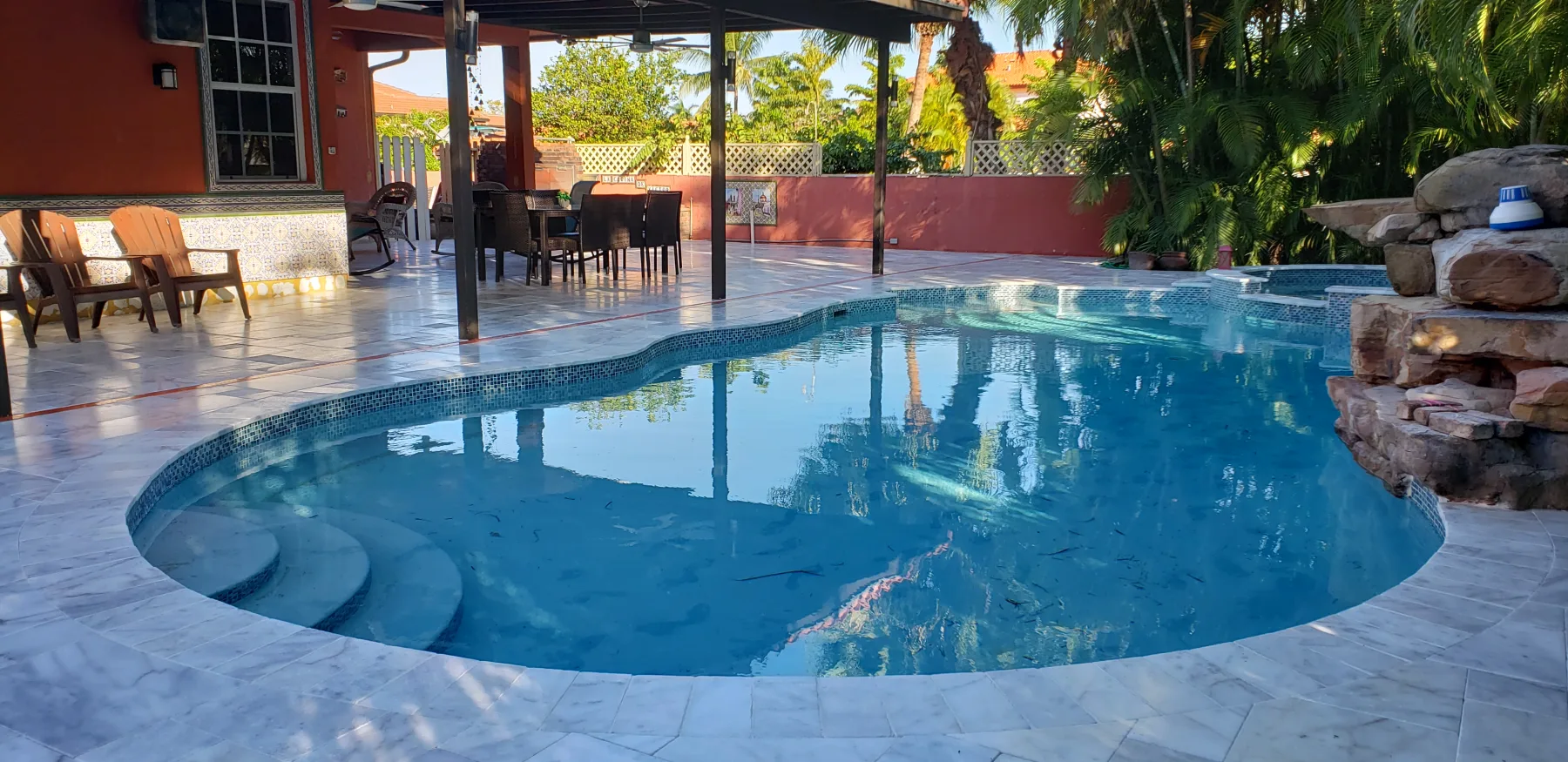 Curved blue swimming pool with stone deck and tropical planting