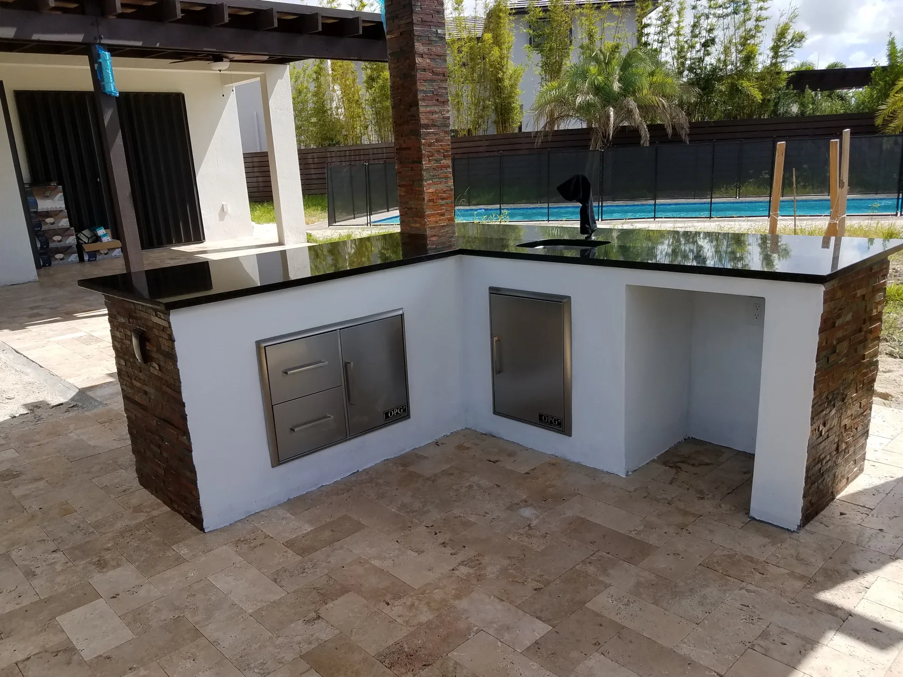White outdoor kitchen island with grill and sink beside a pool