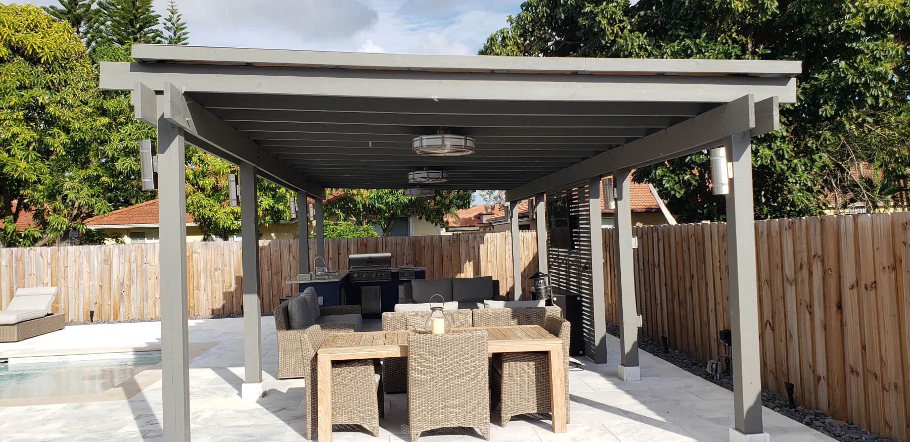 Outdoor dining table under a gray pergola beside the pool